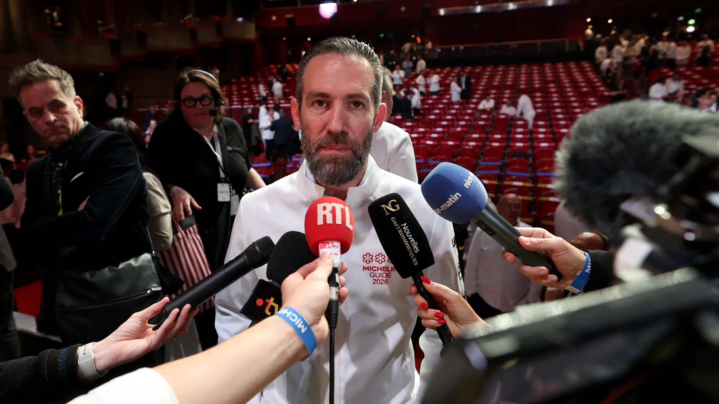 Chef in white Michelin Guide 2026 jacket interviewed by multiple microphones at auditorium event