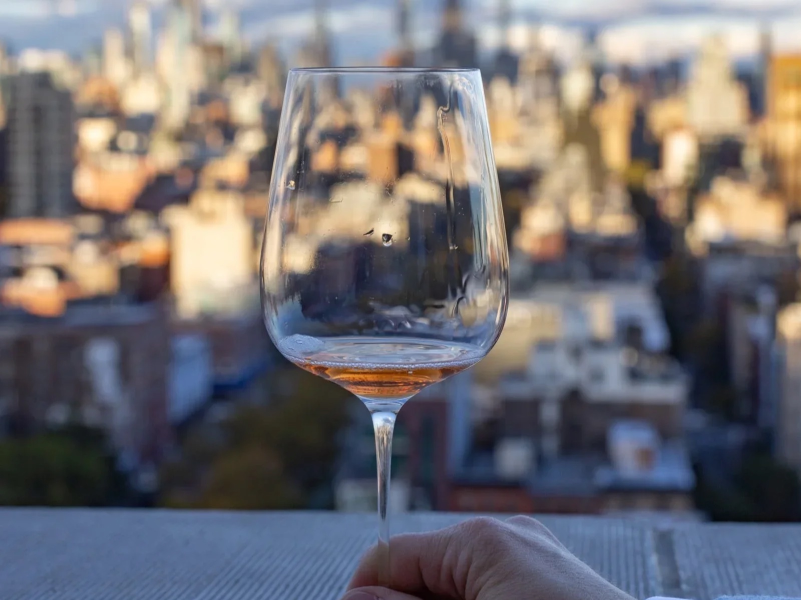 A hand holding a wine glass against the New York skyline.