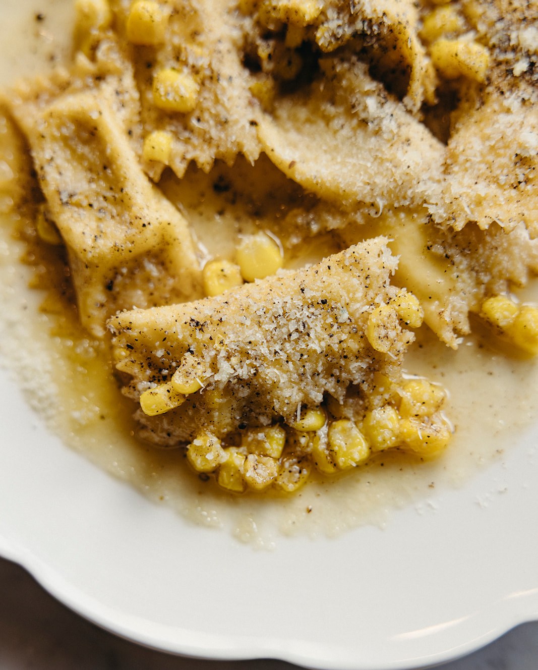 Seasoned corn kernels and sliced meat on a cream-colored plate, topped with coarse salt and black pepper