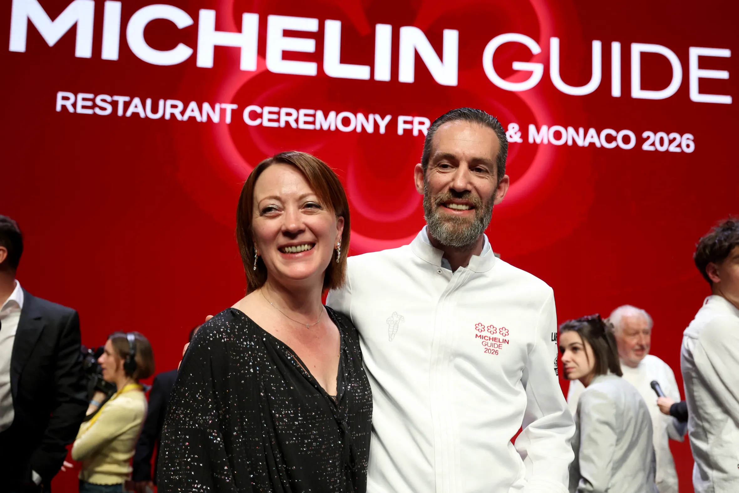 Two people smiling at Michelin Guide 2026 restaurant ceremony event with red backdrop