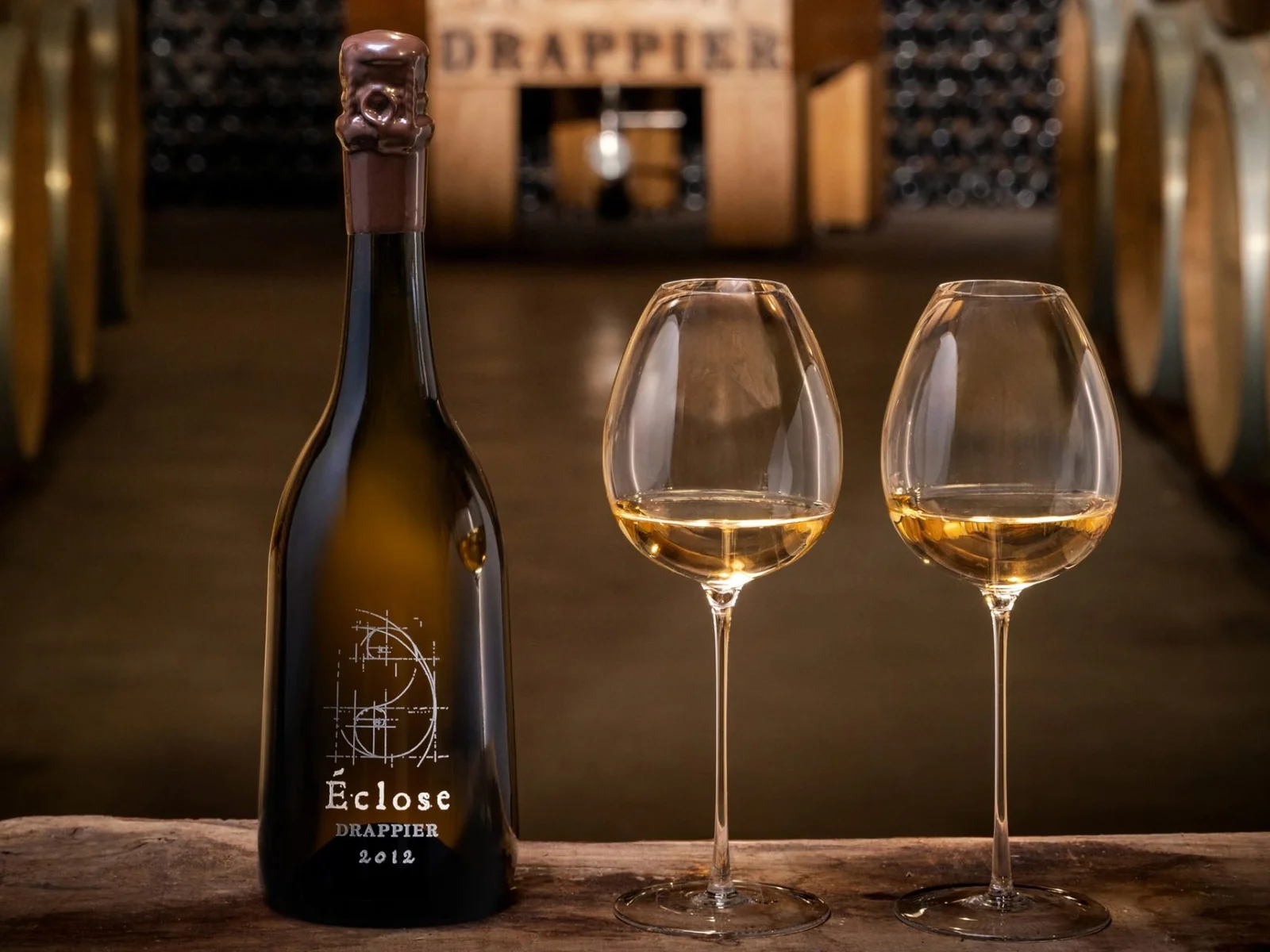 A bottle of Champagne Drappier Éclose 2012 beside two glasses.