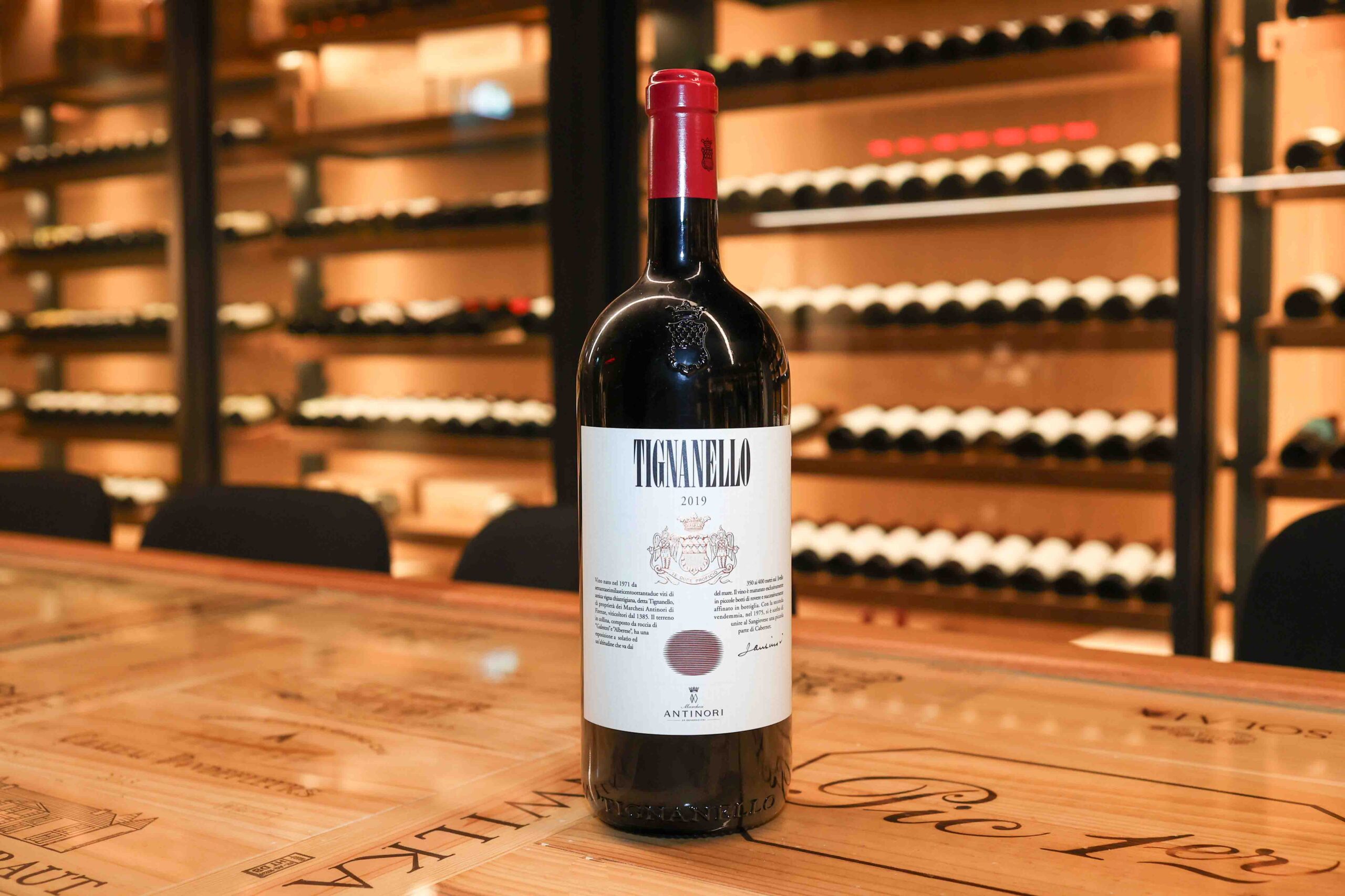 Tignanello 2019 wine bottle with red foil cap on wooden counter in front of wine cellar shelving